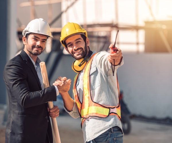 Happy workers at construction site, young civil engineer manager and architects handshaking at construction site and looking to next construction phase  , cooperation teamwork concept.